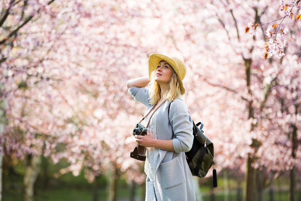 Smiling tourist woman holding camera with spring blooms in background.