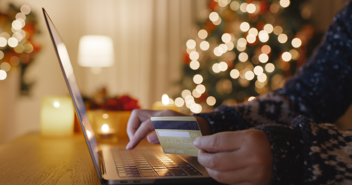 Guest shopping for Hilton holiday deals on a laptop with warm holiday lights glowing in the background.