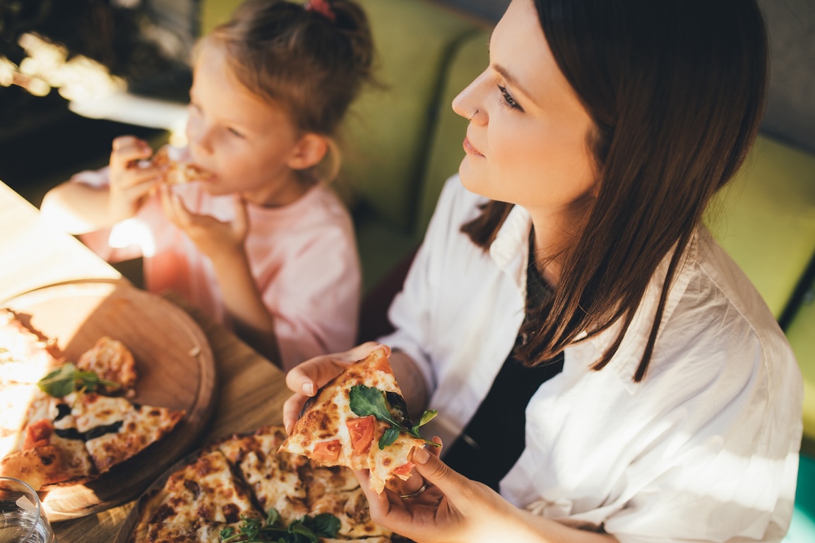 Happy mother and daughter eat pizza in a cafe and having fun.